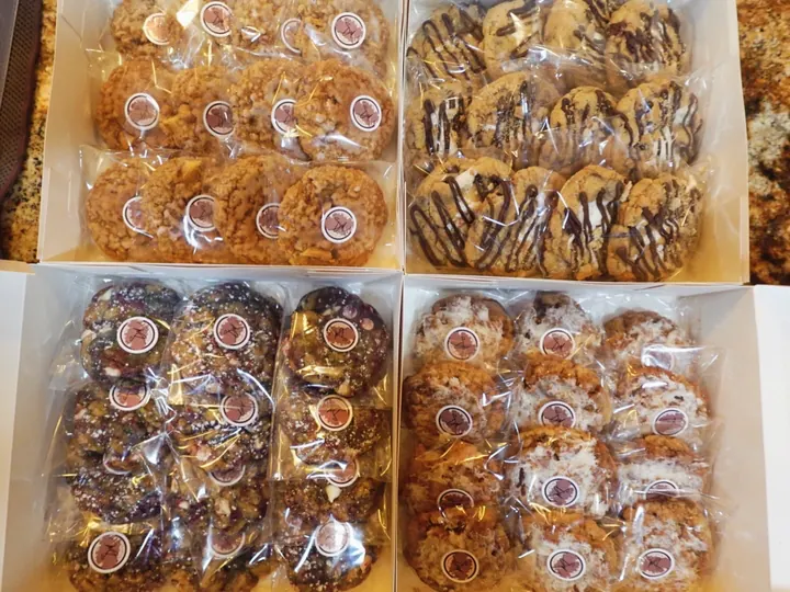 Four white boxes filled with individually wrapped cookies, each sealed with Madison's SM sticker, ready for Bake to Donate orders