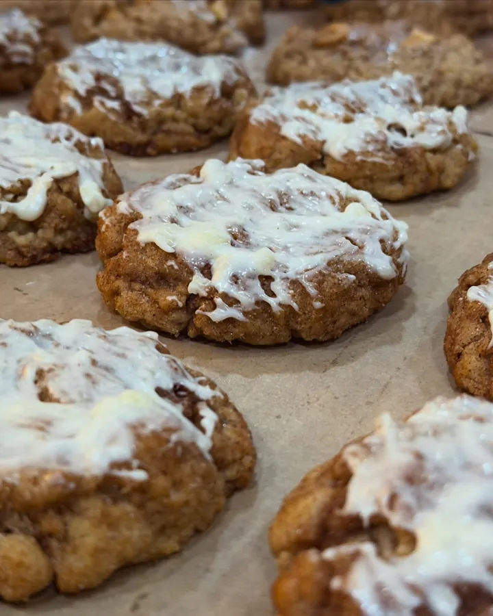 Close-up of Madison's brown butter cookies, dusted with cinnamon sugar and drizzled with white icing, cooling on parchment